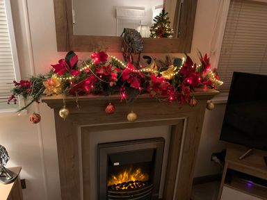 A fireplace decorated with red and gold Christmas ornaments and lights at Lilac Lodge in Carnforth