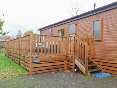 A wooden deck with a railing and stairs attached to a brown cabin at Fountain View in Warton near Carnforth