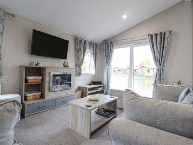 A living room with a mounted television fireplace coffee table and sliding glass doors at Fountain View in Warton near Carnforth