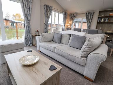A living room with a grey sofa and cushions a wooden coffee table and shelves at Fountain View in Warton near Carnforth