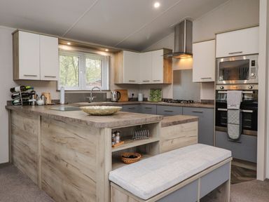 A kitchen with wooden cabinets a window above the sink a built-in oven and microwave and a bench seat at Fountain View in Warton near Carnforth