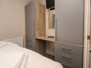 A bedroom with a bed towels on it a radiator and built in wardrobe with a mirror and a television above at Fountain View in Warton near Carnforth