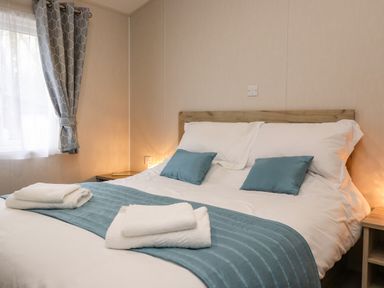 A bedroom with a bed with white sheets blue cushions and towels near a window with curtains at Fountain View in Warton near Carnforth