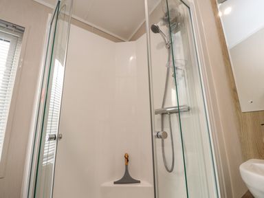 A shower enclosure with glass doors a handheld showerhead a scraper and part of a sink visible at Fountain View in Warton near Carnforth