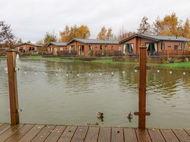 A pond with ducks and wooden cabins in the background at Fountain View in Warton near Carnforth