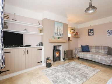 A living room with a plaid sofa a wood burner and a television on a cabinet at Beck View in Sheringham
