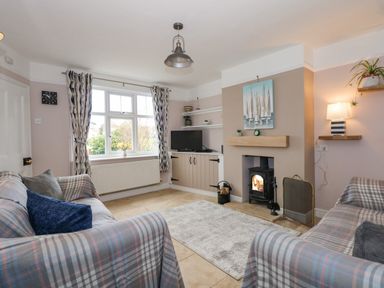A living room with two sofas a fireplace a television on a cabinet and patterned curtains at Beck View in Sheringham