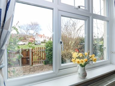 A window with a vase of yellow flowers on the sill overlooking a small garden with a wooden gate at Beck View in Sheringham