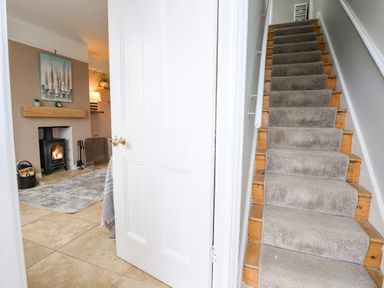 A carpeted staircase next to an open white door showing a living room with a fireplace and wood stove at Beck View in Sheringham