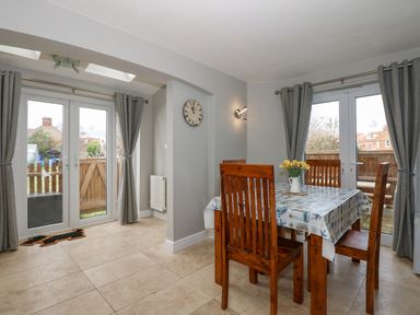 A dining room with wooden table and chairs and glass doors with grey curtains at Beck View in Sheringham