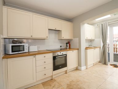 A kitchen with cream cabinets a microwave toaster oven kettle and glass doors with curtains at Beck View in Sheringham