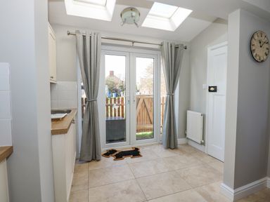 A kitchen area with tiled floor curtains on glass doors and a wall clock at Beck View in Sheringham