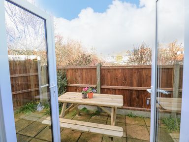 A small outdoor patio with a wooden picnic table and two potted plants surrounded by a wooden fence at Beck View in Sheringham
