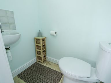 A small bathroom with a toilet sink a wooden storage unit with baskets a soap dispenser and a striped floor mat at Beck View in Sheringham