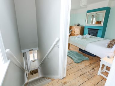 A staircase leading down to a door and an adjacent bedroom with a bed dresser and a mirror above a fireplace at Beck View in Sheringham