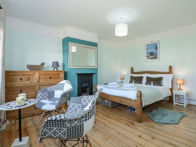 A bedroom with a wooden bed a wooden dresser two patterned chairs and a small round table at Beck View in Sheringham