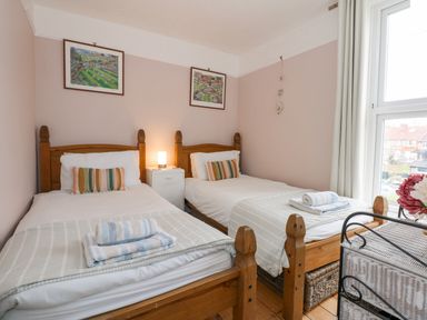 A bedroom with two single beds a small bedside table with a lamp and a window at Beck View in Sheringham