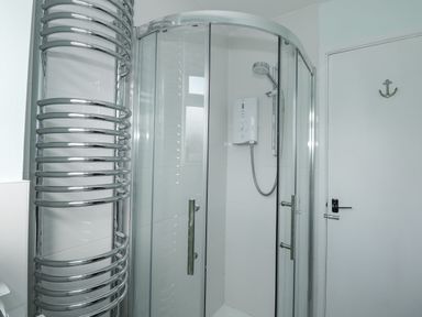 A bathroom shower cubicle with glass doors a wall-mounted shower unit a chrome towel radiator and a white door with an anchor hook at Beck View in Sheringham