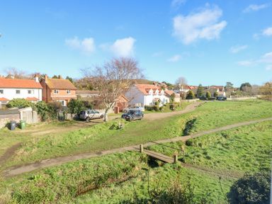A small bridge over a stream in a grassy area near houses and cars at Beck View in Sheringham