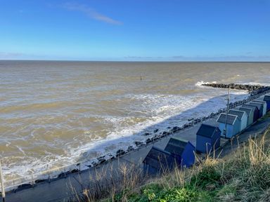 Beach huts along a promenade by the sea with waves and a rocky breakwater at Beck View in Sheringham