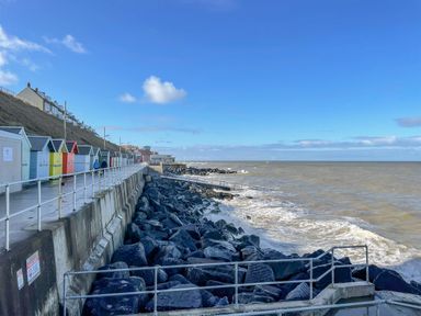 A seaside promenade with colorful beach huts along a cliff and rocky shoreline at Beck View in Sheringham