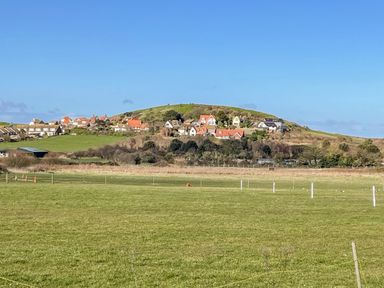 A grassy field with houses on a hill under a clear blue sky at Beck View in Sheringham