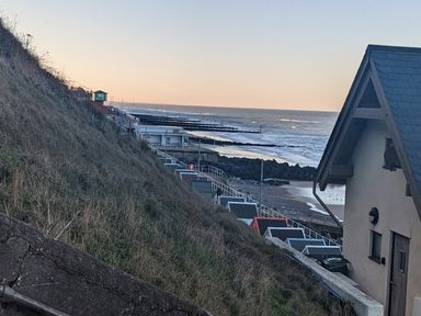 A coastal scene with beach huts near the shore and a building with a slate roof by the sea at Beck View in Sheringham