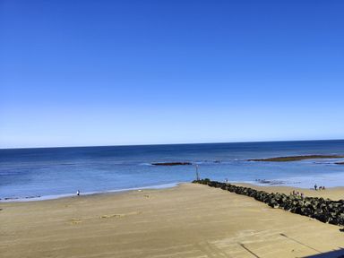 A sandy beach with people walking near the water and a rocky breakwater at Beck View in Sheringham