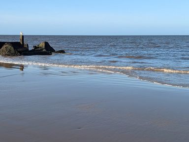 A beach with waves and rocks with a bird standing on a post at Beck View in Sheringham