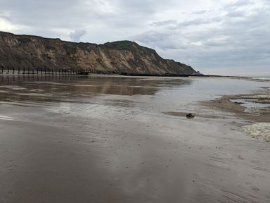 A sandy beach with cliffs in the background and cloudy sky at Beck View in Sheringham