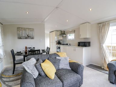 An open plan living room with a grey sofa and yellow cushion a dining table with chairs and a kitchen with white cabinets and appliances at 11 Mansion View in Helensburgh near Kilcreggan