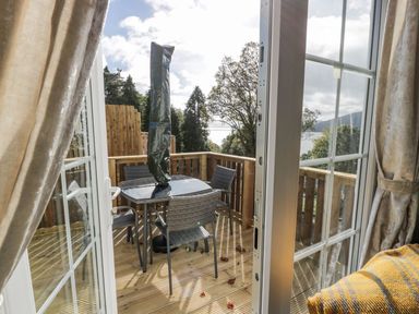 A balcony with a table and four chairs surrounded by wooden railings and trees visible through open glass doors at 11 Mansion View in Helensburgh near Kilcreggan