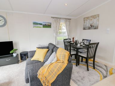 A living room with a gray sofa and yellow throw next to a dining table set with plates glasses and cutlery at 11 Mansion View in Helensburgh near Kilcreggan