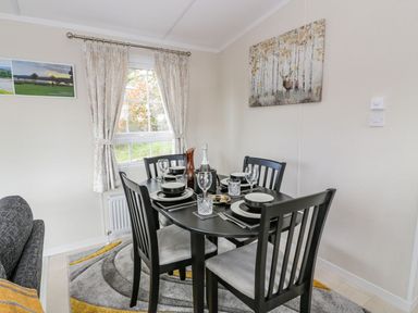 A dining area with a black table set for four including plates glasses and cutlery near a window with curtains and a painting on the wall at 11 Mansion View in Helensburgh near Kilcreggan