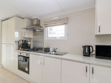 A kitchen with white cabinets a stovetop a sink a black kettle and a window at 11 Mansion View in Helensburgh near Kilcreggan