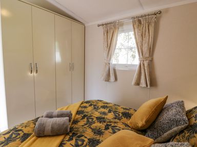A bedroom with a bed covered in yellow and black bedding with towels on it and a window with curtains at 11 Mansion View in Helensburgh near Kilcreggan