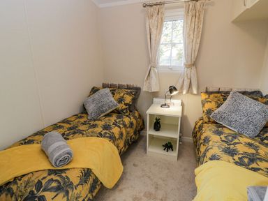 A bedroom with two single beds separated by a white bedside table with a lamp and decorative items at 11 Mansion View Helensburgh near Kilcreggan