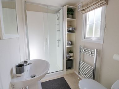 A bathroom with a sink, shower cabin, shelving with towels and plants, a towel radiator and a window at 11 Mansion View Helensburgh near Kilcreggan
