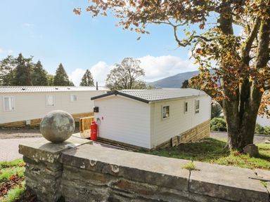 Two white mobile homes near a stone wall and large tree with hills in the background at 11 Mansion View Helensburgh near Kilcreggan