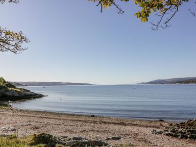 A pebbled beach with calm water and distant hills under a clear sky at 11 Mansion View in Helensburgh near Kilcreggan