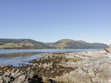 A rocky shoreline with water and hills in the background at 11 Mansion View in Helensburgh near Kilcreggan