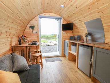 A wooden pod interior with a small kitchen area and dining table with stools at Parys Pod in Amlwch