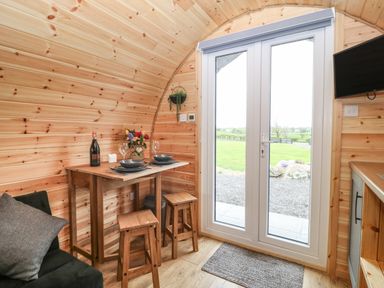 A small dining table with two stools near glass doors in a wooden cabin at Parys Pod in Amlwch