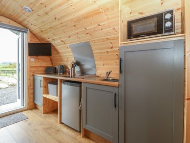 A small kitchen area with a microwave fridge toaster kettle and sink at Parys Pod in Amlwch