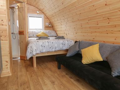A wooden room with a bed near a window and a black sofa with cushions at Parys Pod in Amlwch