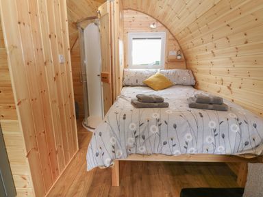 A bedroom with a bed linens and towels on a bed a window and a shower in a wooden pod at Parys Pod in Amlwch