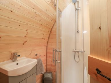 A small bathroom with a sink cabinet shower with glass door and wooden walls at Parys Pod in Amlwch