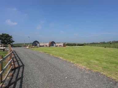 A gravel driveway leading to two small wooden pods on a grassy field at Parys Pod in Amlwch