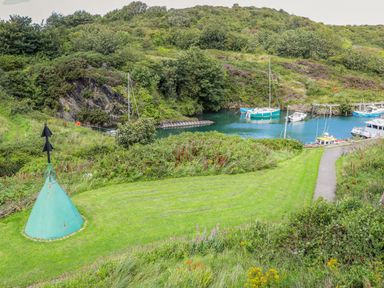 A small harbor with boats docked surrounded by grassy hills and a path near Parys Pod in Amlwch
