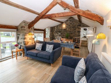 A living room with blue sofas wooden beams stone walls and a dining table with chairs at Y Bwthyn in Dyffryn Ardudwy
